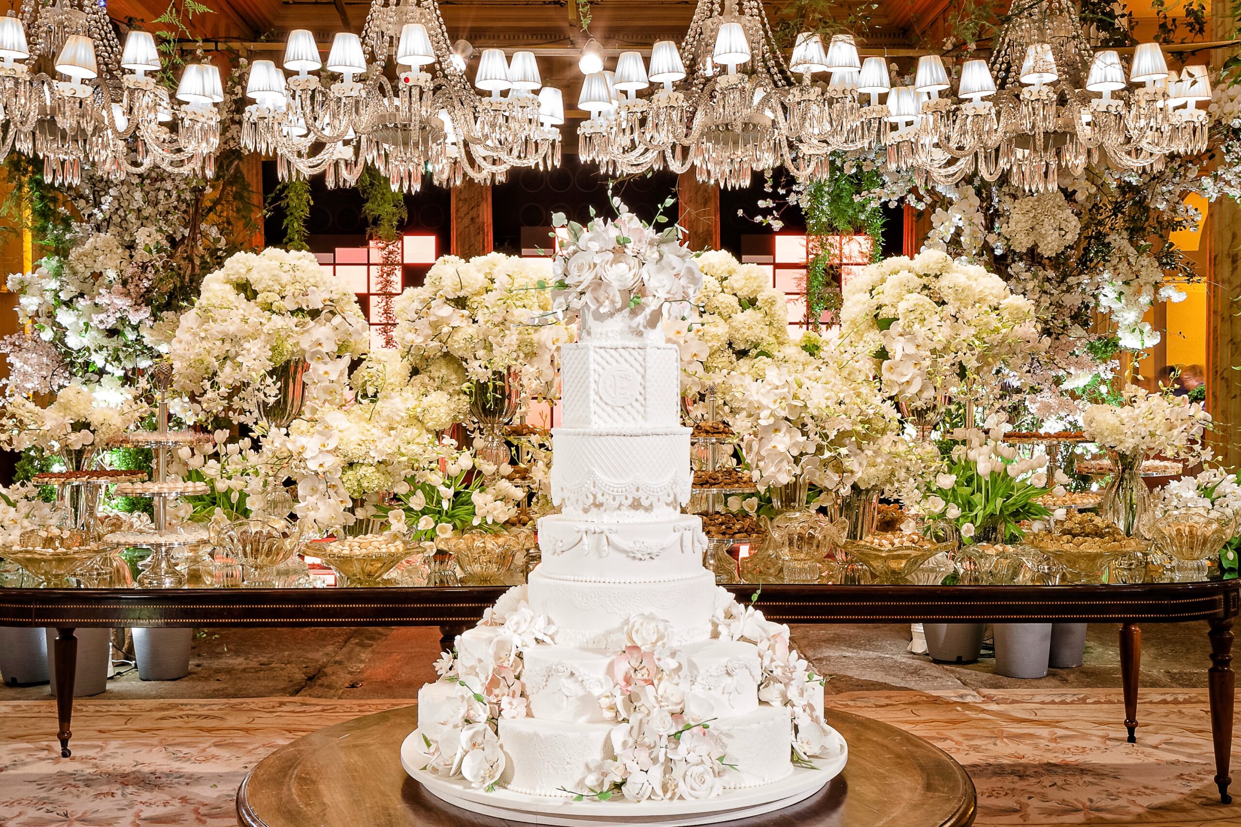 Mesa de doces ganha destaque com bolo monumental e arranjos florais brancos. | Foto: Divulgação