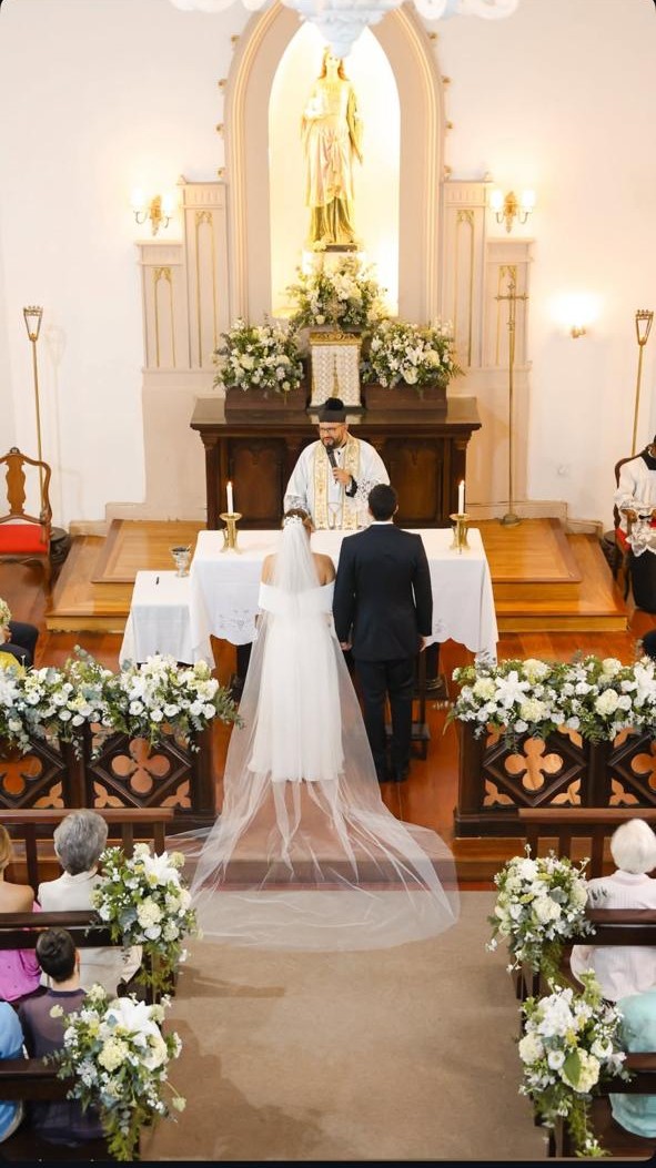 Noivos acompanham celebração diante do altar em igreja