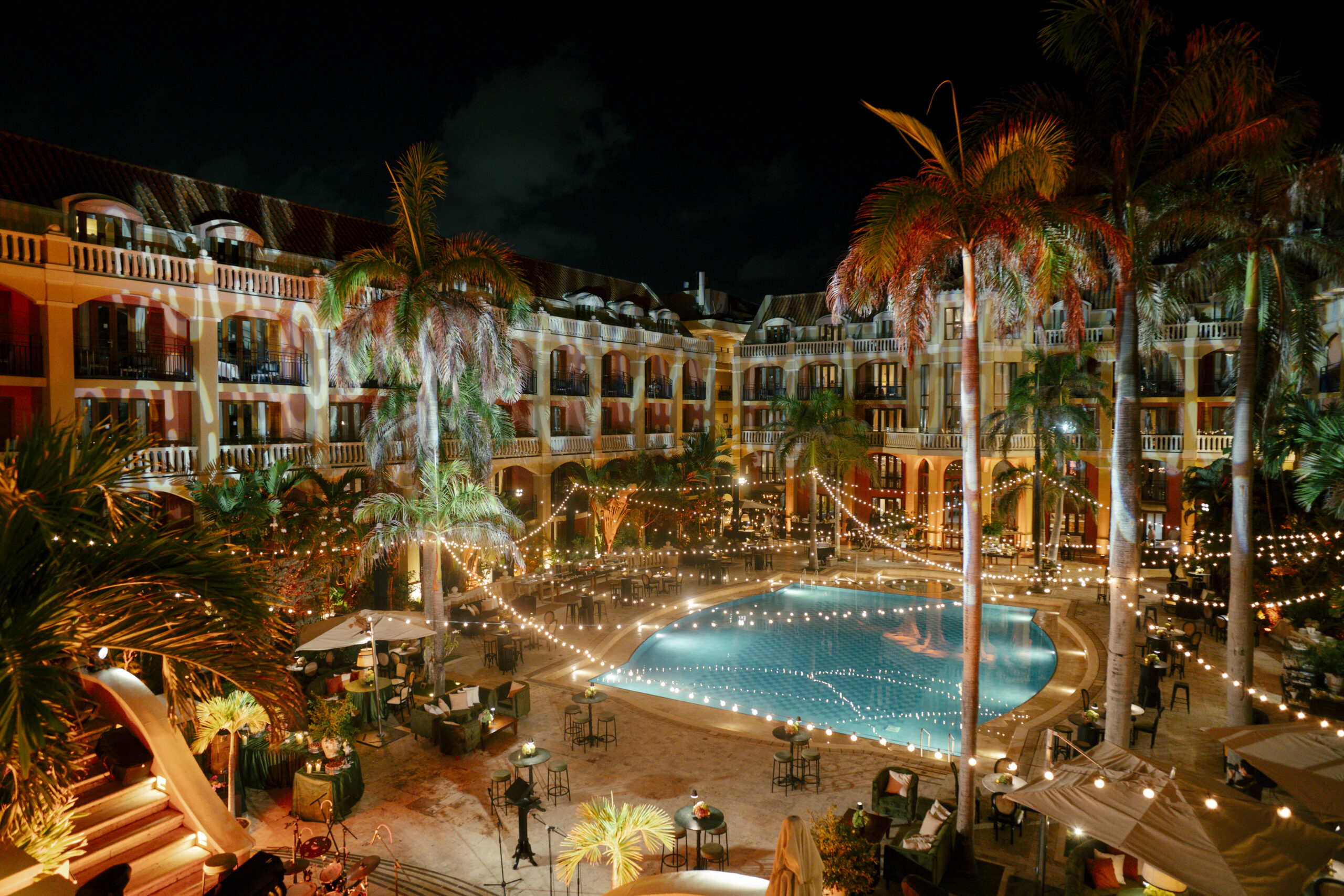 Área externa do Sofitel Legend Santa Clara recebe ambientação noturna com iluminação suspensa, mesas de convivência e piscina central, em cenário preparado para uma das experiências do evento.