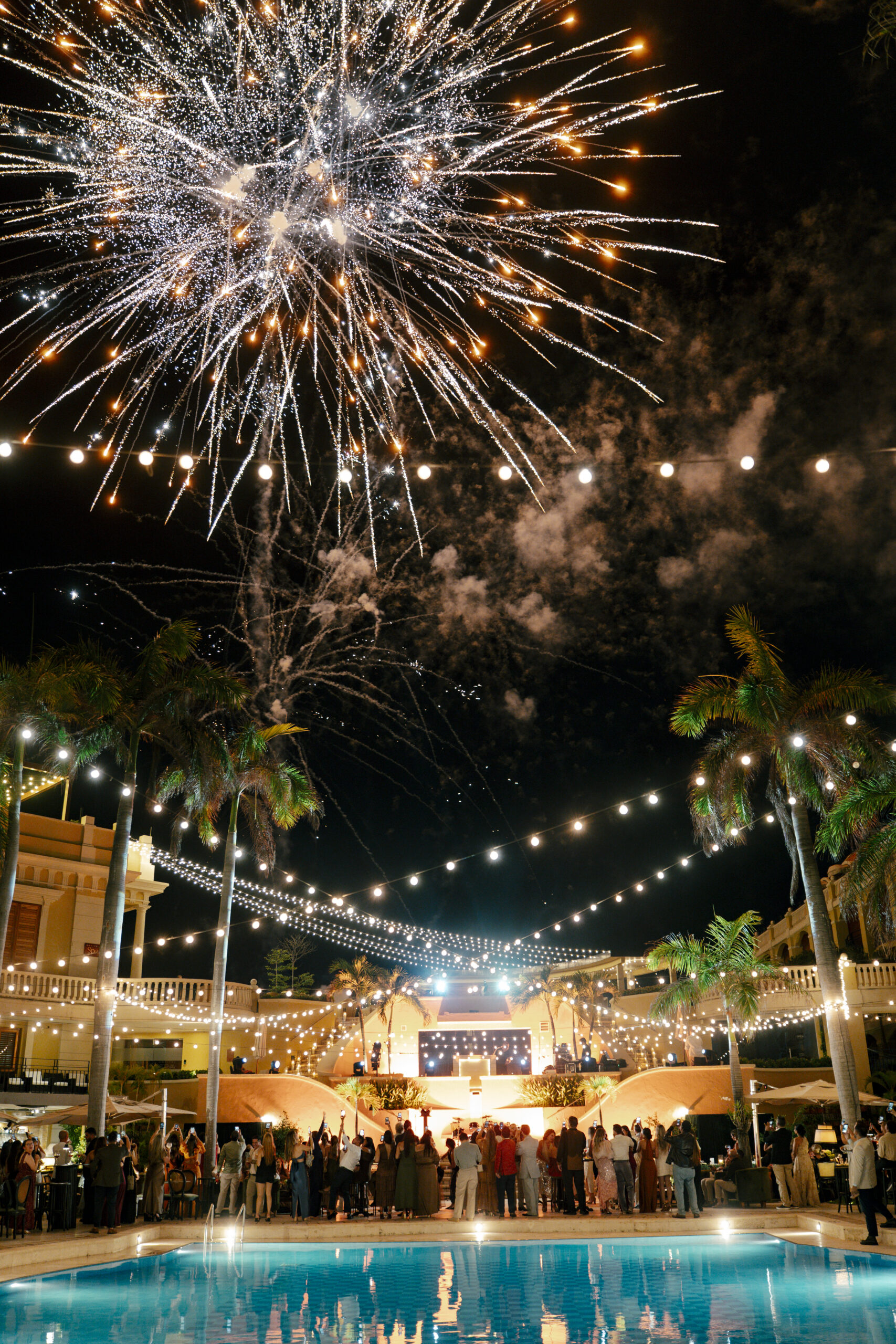 Queima de fogos de artifício ilumina o céu de Cartagena durante uma celebração ao ar livre, realizada em um espaço com arquitetura histórica e iluminação decorativa.