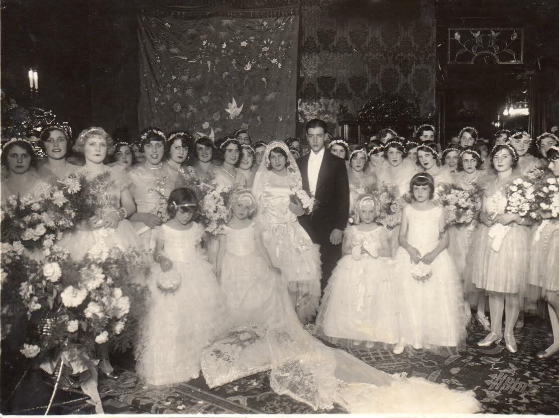 Flora Camargo e Bento Munhoz da Rocha Netto, em Curitiba, em 1929. O casal aparece cercado pelas participantes do cortejo, que usam vestidos claros e carregam buquês. O registro documenta um casamento da elite paranaense.I Foto: Acervo Curitiba Histórica / Paraná Histórica.