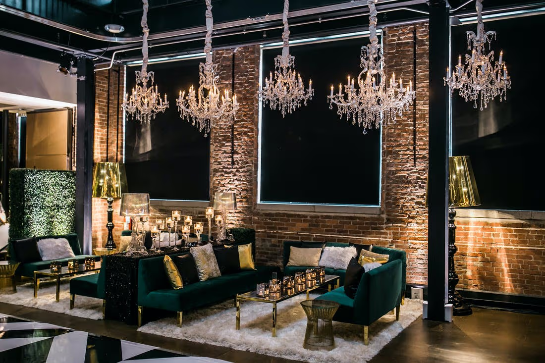 Ambiente sofisticado que combina tijolos aparentes, lustres de cristal, sofás de veludo verde e detalhes dourados em uma atmosfera elegante e acolhedora. I Foto: Party Slate