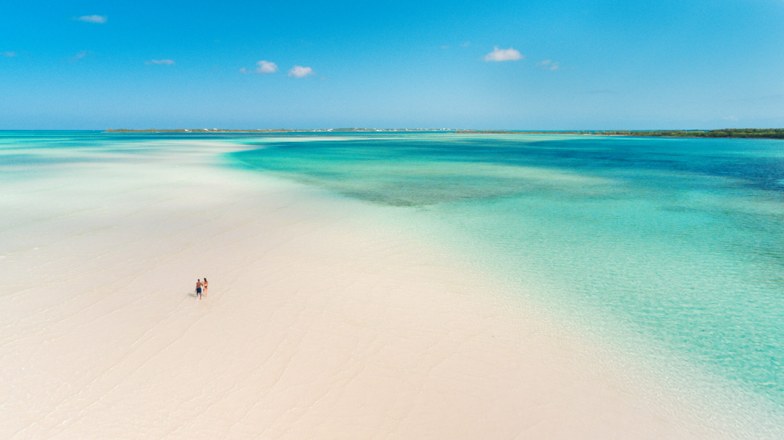 Vista aérea mostra casal caminhando por extenso banco de areia cercado por águas cristalinas nas Bahamas. | Foto: The Bahamas Ministry of Tourism (BMOT)