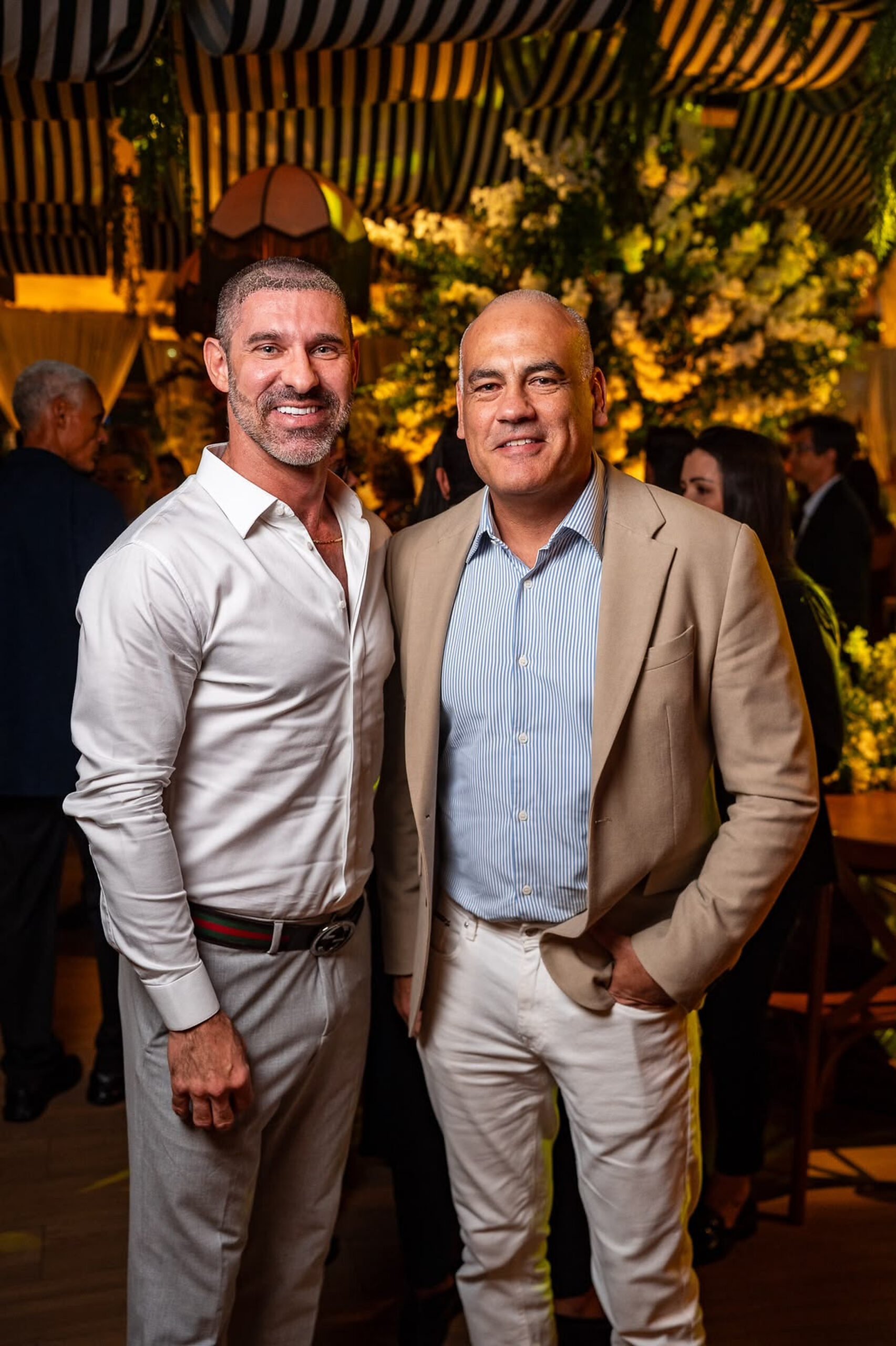 Claudio Tironi e Fabiano Niederauer posam durante a Première Inesquecível, com a decoração floral do Ballroom Beach Club ao fundo. | Foto: Chris Machado
