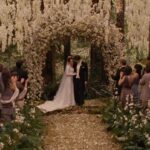 Bella e Edward celebram a união sob um arco coberto por flores brancas, enquanto os convidados acompanham a cerimônia em um ambiente cercado pela vegetação. Reprodução/Paris Filmes