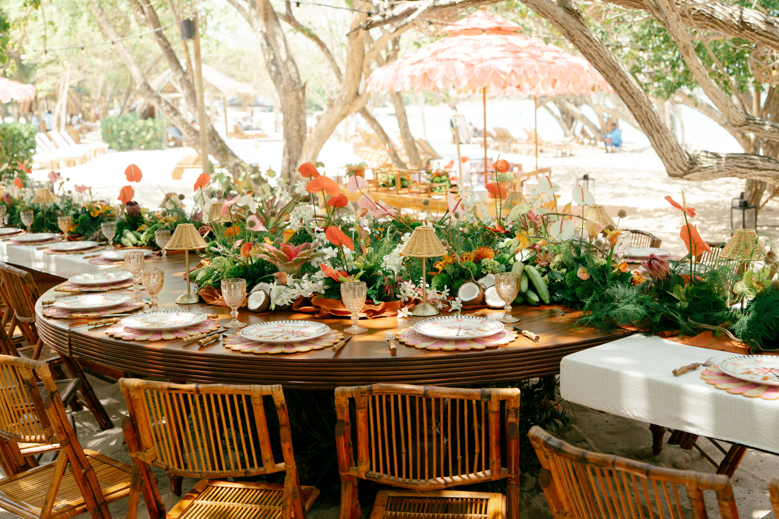 Mesa de formato orgânico reúne arranjos tropicais, antúrios, folhagens, louças decoradas e cadeiras de bambu em uma ambientação ao ar livre | Foto: Compañía Audiovisual