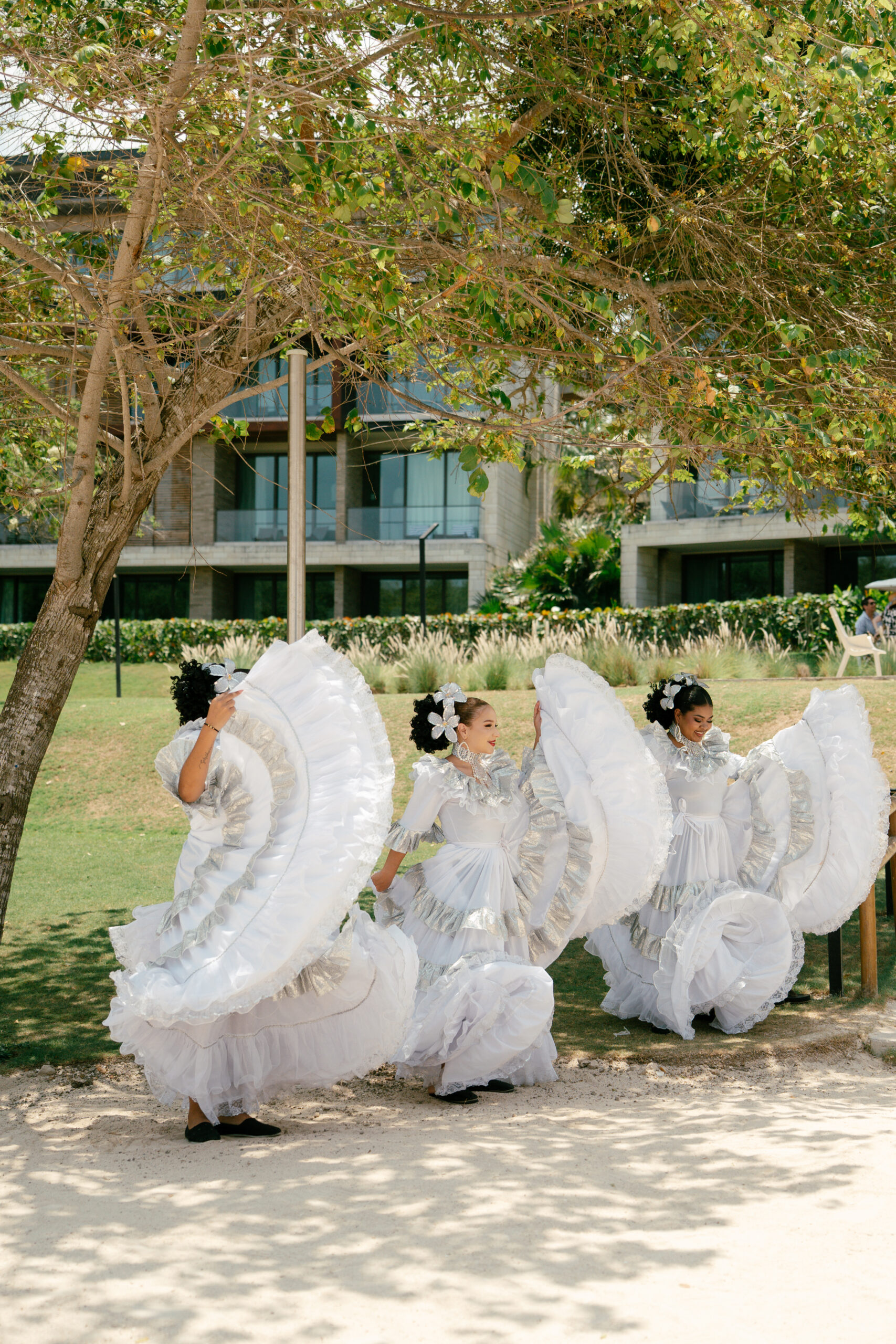 Dançarinas com vestidos brancos volumosos e detalhes prateados realizam apresentação cultural em uma área ajardinada durante a programação do evento | Foto: Compañía Audiovisual
