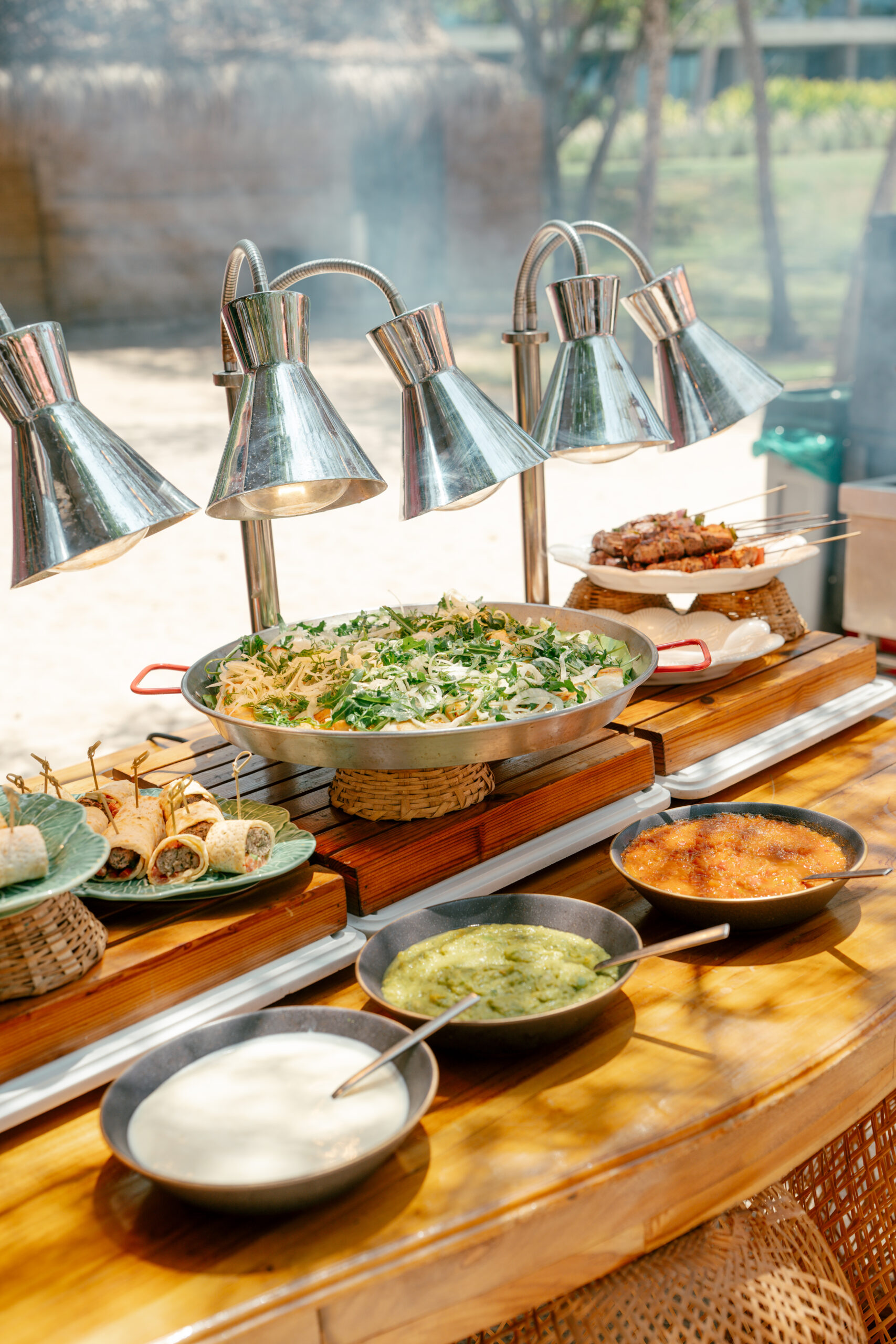 stação gastronômica ao ar livre apresenta diferentes preparações, acompanhamentos e molhos, servidos em uma estrutura de madeira com luminárias aquecedoras | Foto: Compañía Audiovisual