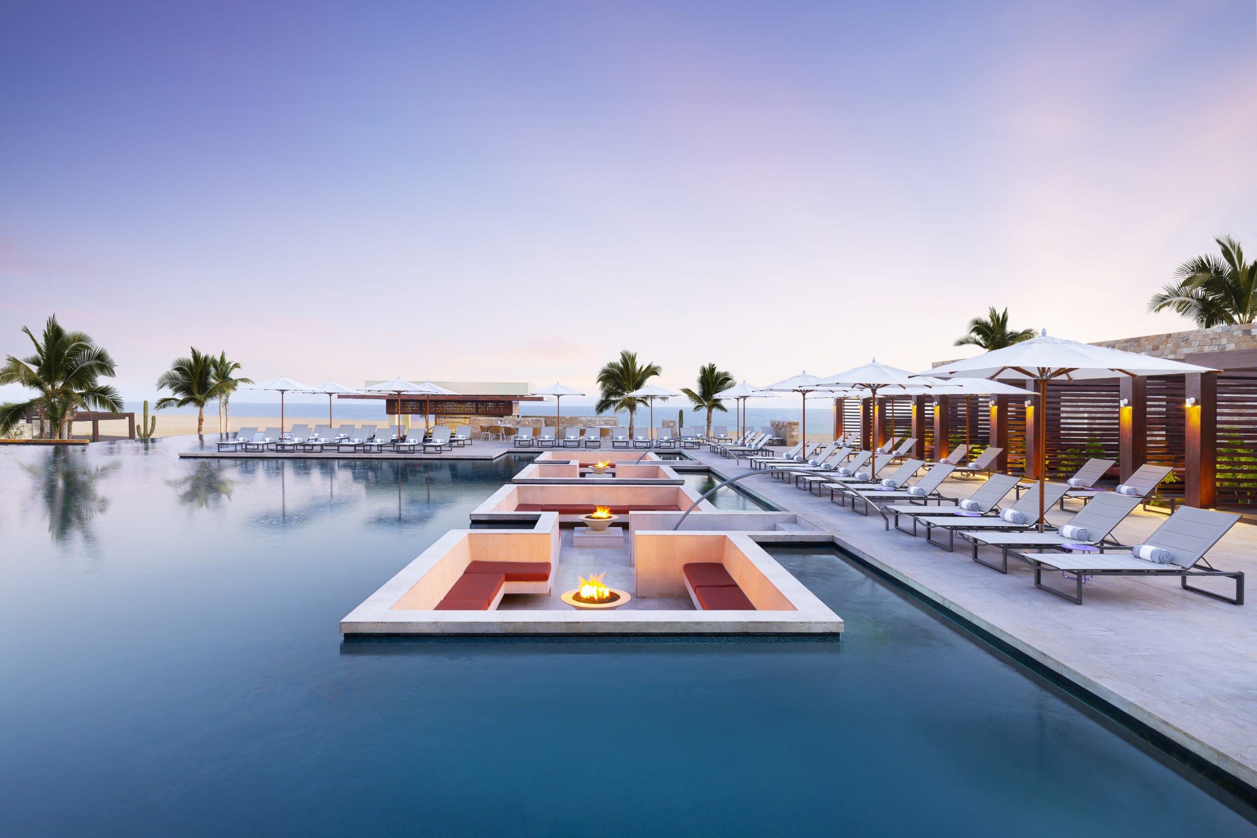 Piscina do resort ao entardecer, com espaços de descanso dentro d'água e vista para o mar. | Foto: Divulgação / Hard Rock Hotel Los Cabos