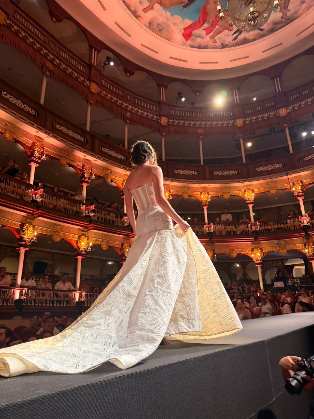Modelo apresenta vestido de noiva estruturado, com saia volumosa e cauda longa, durante desfile realizado em um teatro histórico de Cartagena | Foto: Compañía Audiovisual