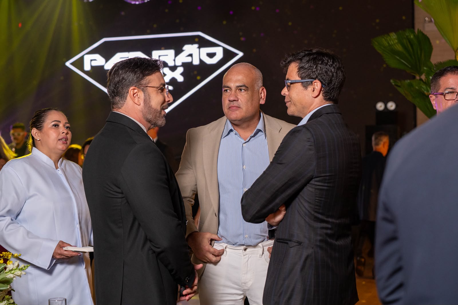 Carlos Junior, Fabiano Niederauer e Davidson Dalcin se reúnem durante o lançamento do Ballroom Beach Club, com a identidade visual de Pedrão Sax ao fundo. | Foto: Chris Machado