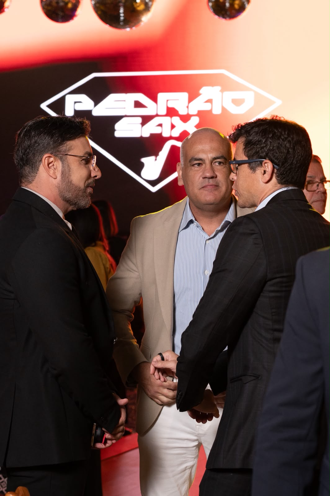 Carlos Junior, Fabiano Niederauer e Davidson Dalcin conversam durante a Première Inesquecível, diante de um painel com a marca Pedrão Sax. | Foto: Chris Machado
