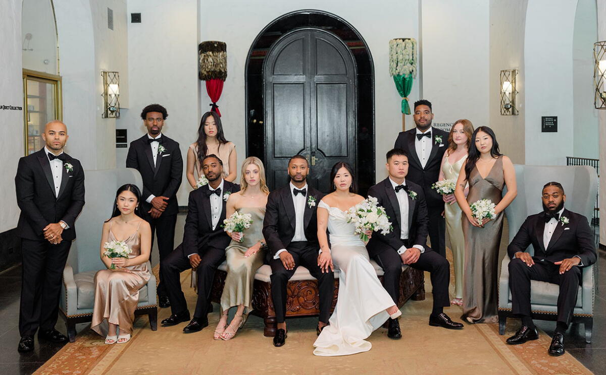 Noivos e padrinhos posam para fotografia em uma composição de trajes black tie, com smokings pretos, gravatas-borboleta e vestidos em tons neutros e metalizados. | Foto: Emily M Choi