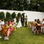 Cerimônia de casamento intimista realizada ao ar livre, em um jardim, com convidados acomodados em cadeiras de madeira e decoração delicada em tons de branco. | Foto: Nina Vilas Boas e Cheng NV