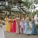 Noiva surpreende as madrinhas durante o first look, momento marcado pela emoção e pelas reações das convidadas, que usam vestidos longos em diferentes cores, formando uma paleta diversificada com tons de amarelo, laranja, rosa, lilás, azul e verde. | Foto: Laís Torres Fotografia