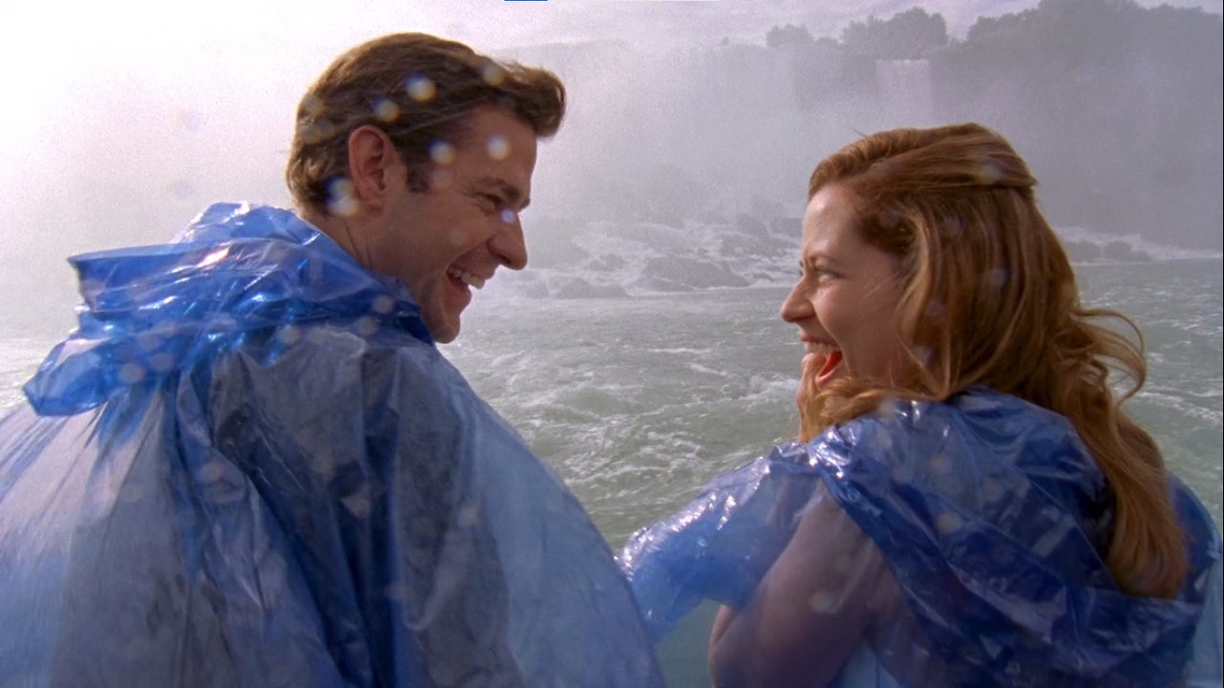 Jim e Pam compartilham um momento de descontração durante o passeio de barco pelas Cataratas do Niágara, usando capas de chuva azuis para se proteger da água. | Reprodução/NBC