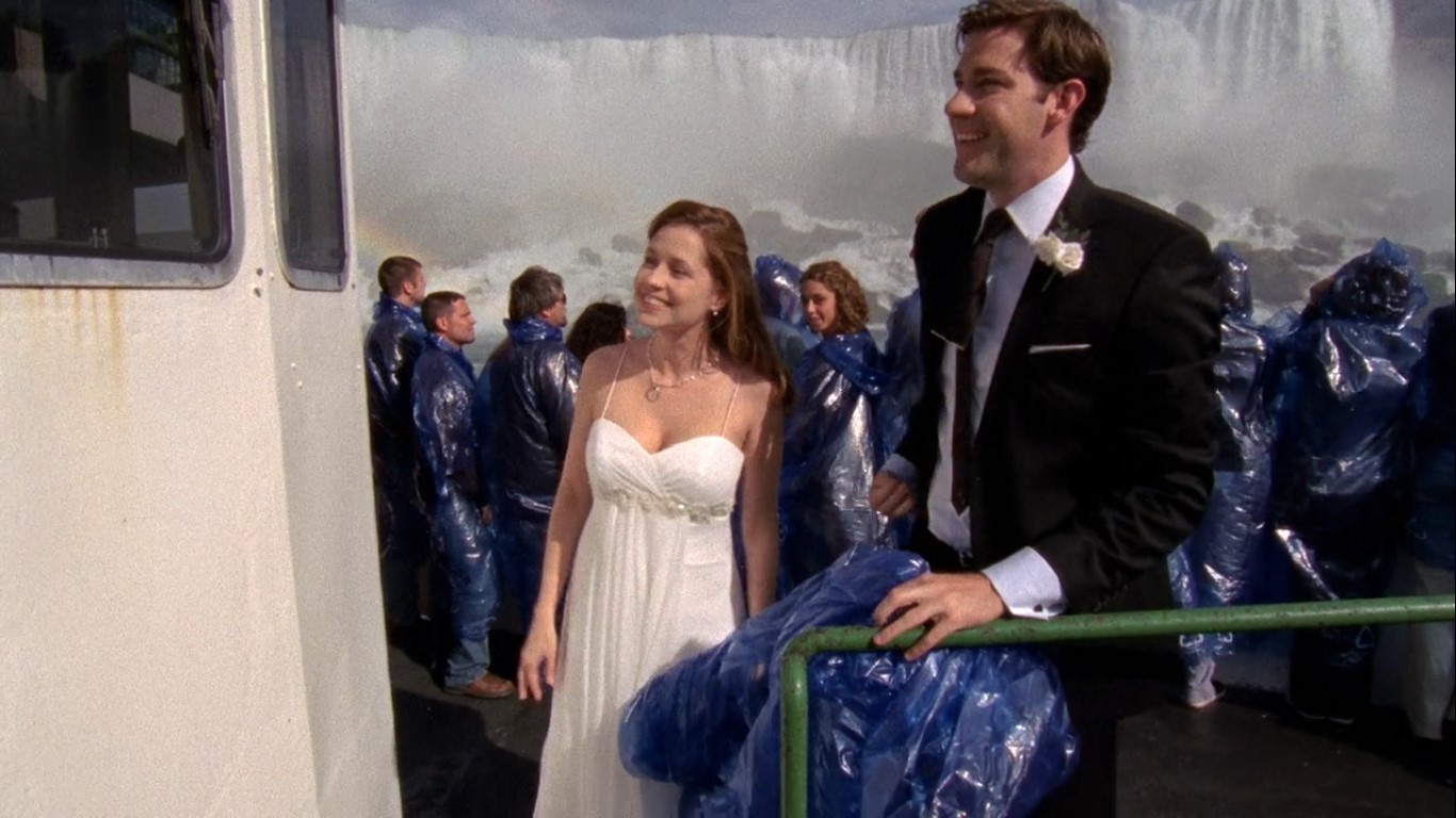 Na realização da cerimônia particular no barco, Jim e Pam aparecem com seus trajes de casamento. Pam usa um vestido branco de alças finas, com modelagem leve e detalhes delicados na cintura. | Reprodução/Paris Filmes
