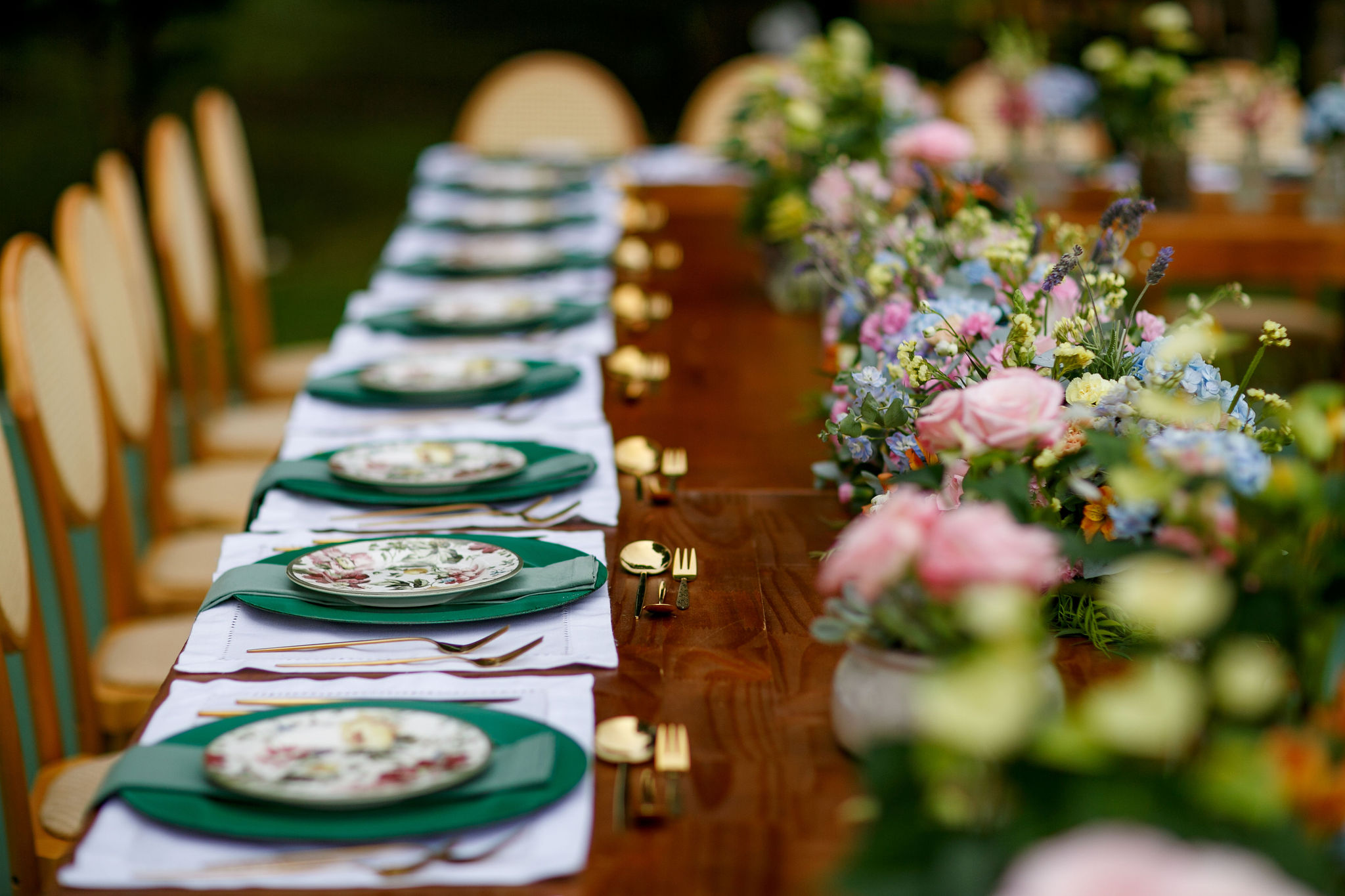 Mesa de recepção decorada com arranjos florais coloridos, louças estampadas, guardanapos verdes e talheres dourados, criando uma composição romântica e acolhedora. | Foto: Nina Vilas Boas e Cheng NV